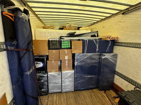 Loaded moving truck with wrapped furniture, boxes, mattresses, and packing pads.