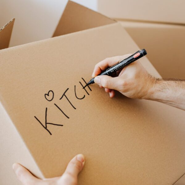 Person using a black marker to label a cardboard moving box with the word KITCHEN